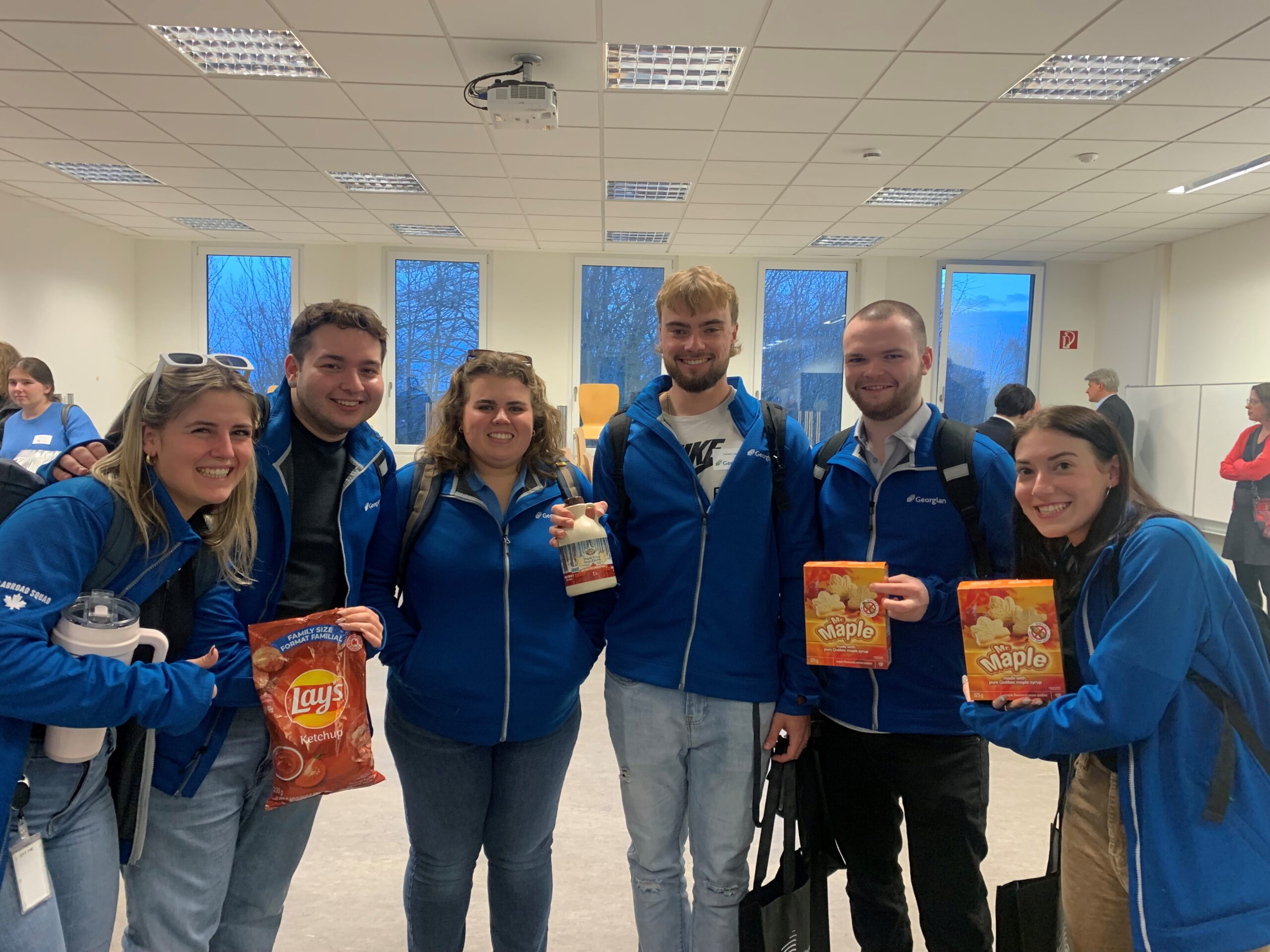 Georgian students in blue Georgian jackets holding Canadian treats for International Flavours activity.